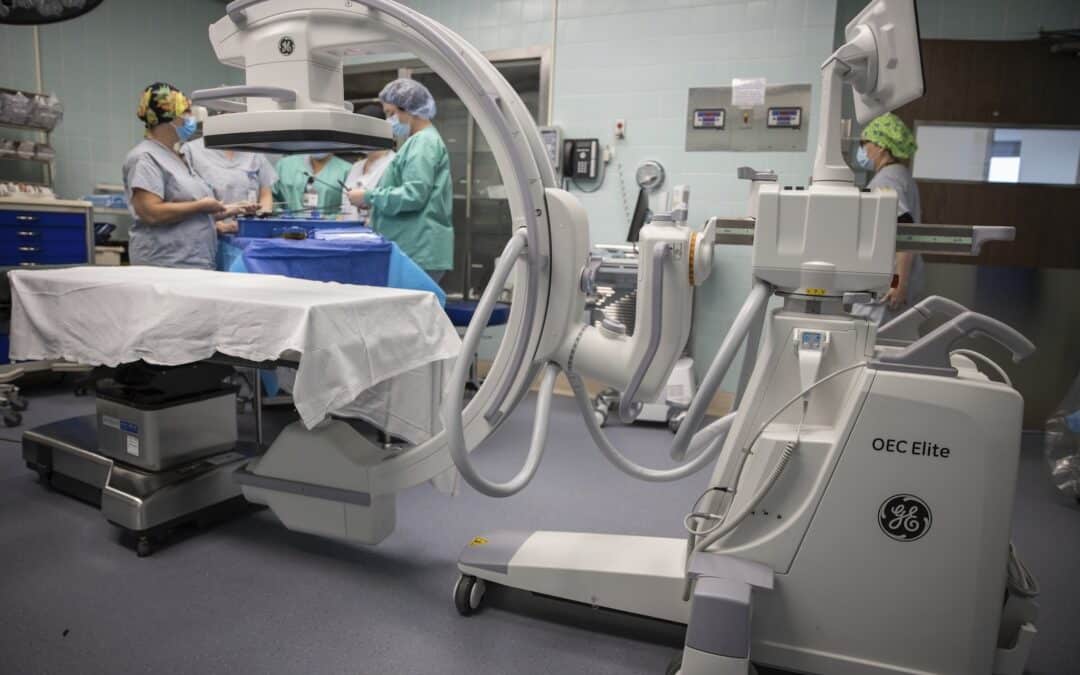 Large medical device over a hospital bed with a group of nurses in the background
