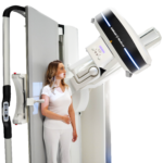 Woman in white standing beside an mri scanner, looking at the machine near the bed. (informative)