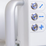 Close-up of a white medical device control panel with blue-lit circular knobs and directional arrows on the right side of the unit.