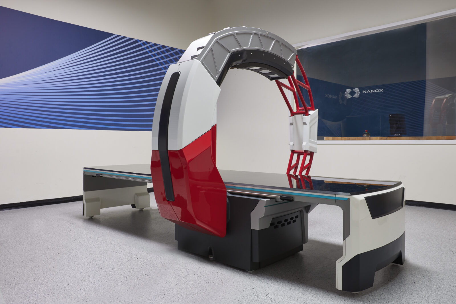 Medical imaging scanner with a circular gantry and red support frame in a showroom, nanox logo visible on a blue wall behind it. “