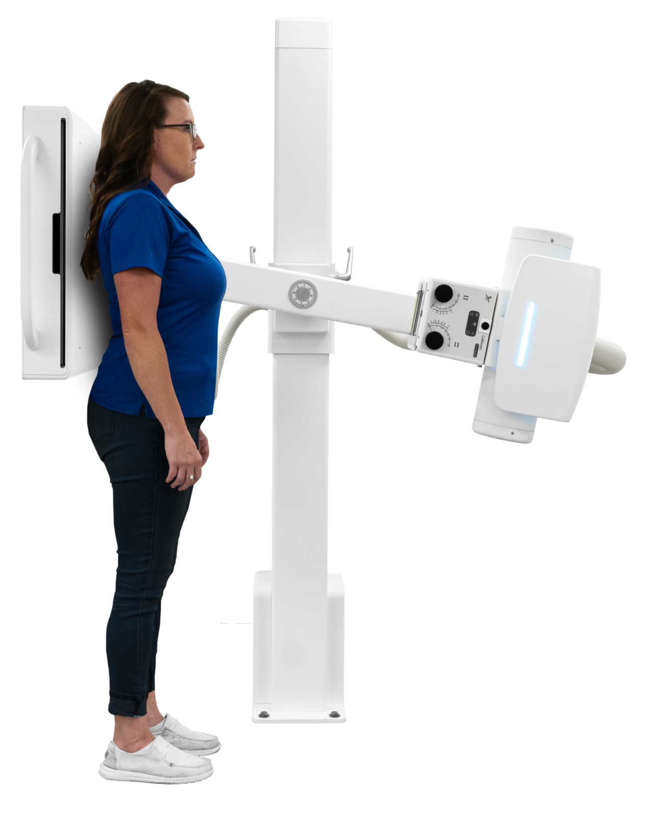 Woman in blue shirt stands beside a tall white medical imaging machine with an adjustable arm/gantry.