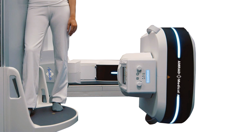 Medical linear accelerator in a radiotherapy setup, with a patient standing on the treatment platform beside the machine labeled amrad medical.