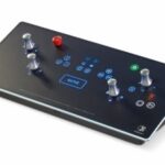 Angled black control panel with several blue-lit buttons, four silver knobs, and a red pushbutton.