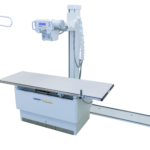 Medical radiography setup with a ceiling-mounted c-arm fluoroscope over an adjustable patient table.