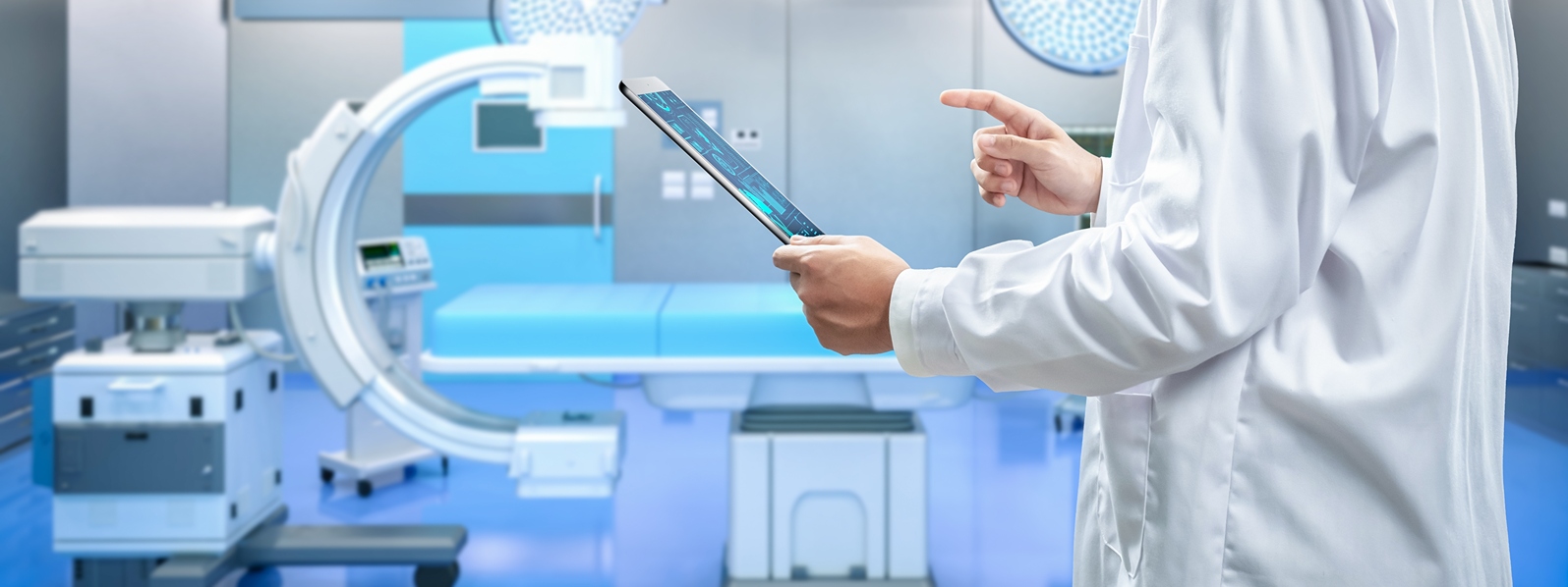 Imit-home-c-arm - Imperial Imaging Technology Medical professional in a white coat uses a tablet in a high-tech radiology suite with a c-arm scanner nearby