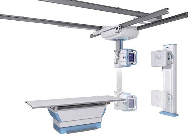 Ceiling-mounted radiography system with a movable gantry over an exam table and wall-mounted control panels.