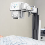 Medical imaging device (x-ray/fluoroscopy) positioned over a patient lying on an examination bed for a radiographic exam
