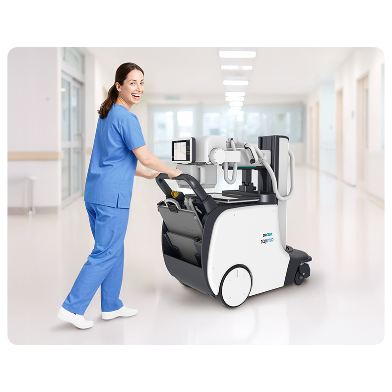 Nurse in blue scrubs pushes a medical imaging robot cart through a bright hospital corridor.