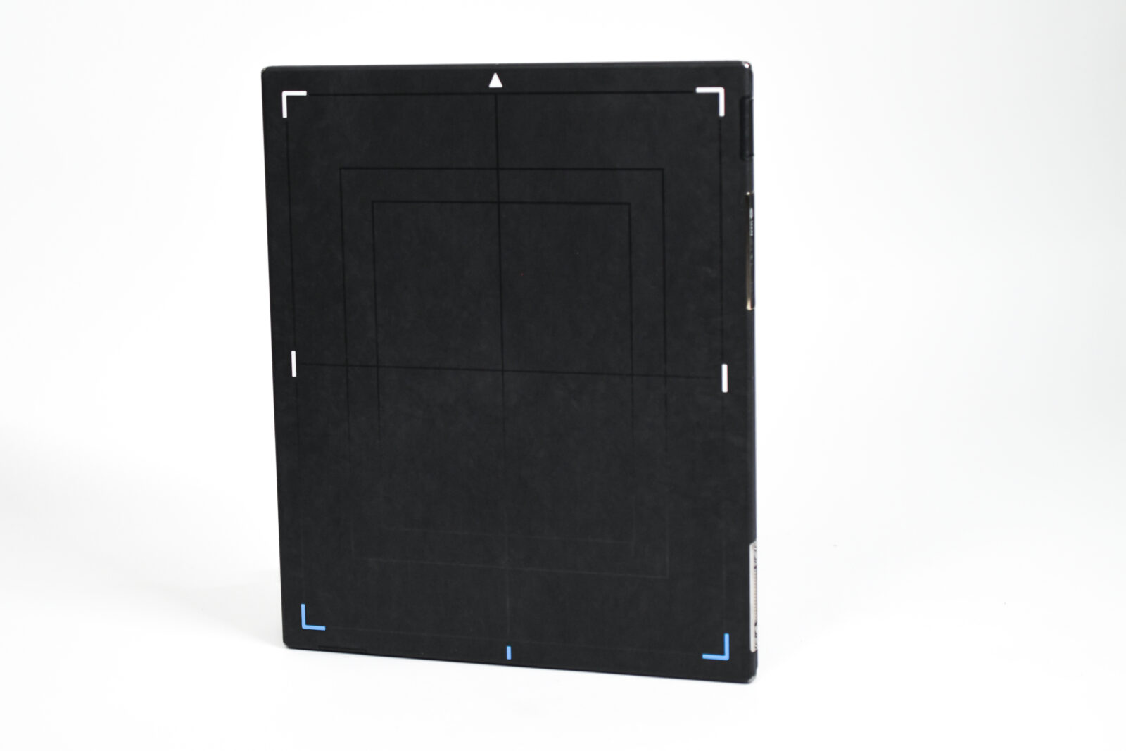 Tall black rectangular box standing on a white surface with white corner markings and blue accents at the bottom edge against a white background.