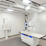 Ceiling-mounted radiography gantry over a patient exam table in a medical imaging room