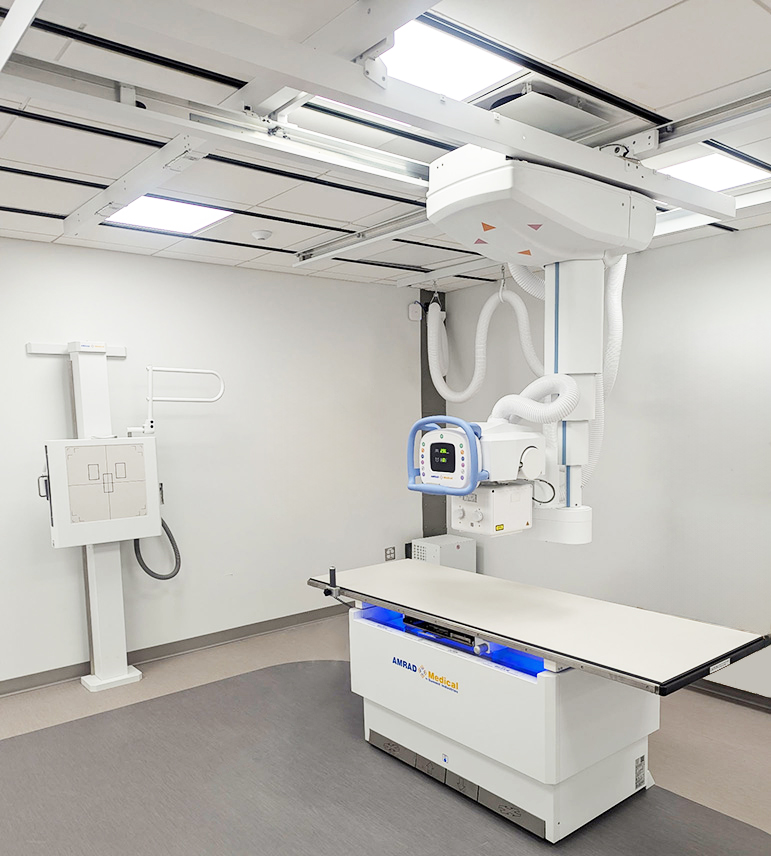 Ceiling-mounted radiography gantry over a patient exam table in a medical imaging room