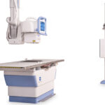 Radiology suite with a patient x-ray table, a ceiling-mounted x-ray unit, and a vertical image receptor on a stand.