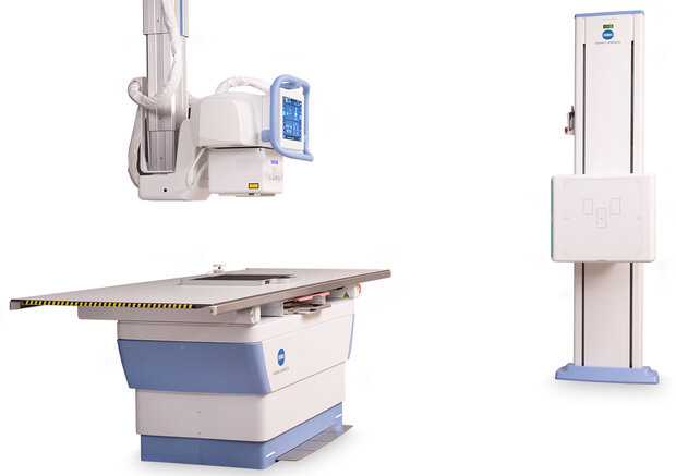 Radiology suite with a patient x-ray table, a ceiling-mounted x-ray unit, and a vertical image receptor on a stand.