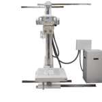 Vertical radiography stand with an overhead arm and patient table, used for x-ray imaging in medical exams, with control panel on the upright column and cables connected to a separate unit.
