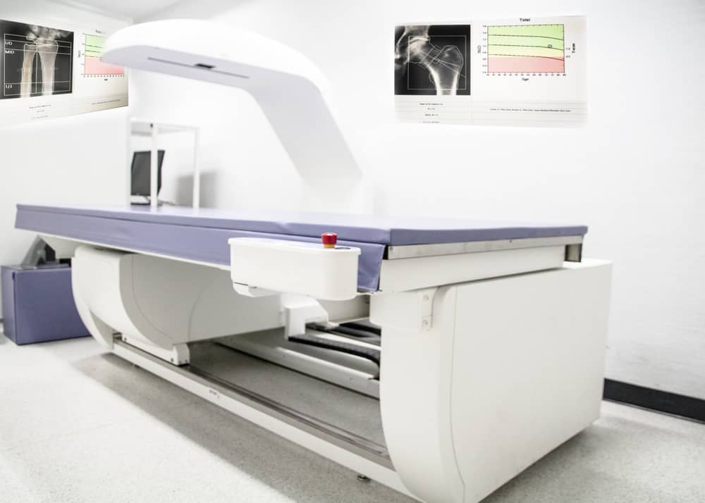 Radiology ct/mri scanner with an examination table in a bright, empty imaging room with wall charts on display.