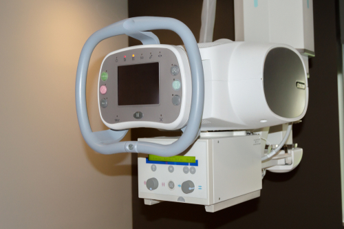 Medical imaging device (c-arm fluoroscopy unit) with control panel and screen mounted on a wall/stand, used for x-ray imaging during procedures.