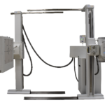 Industrial x-ray imaging gantry with vertical columns and horizontal beam arms, connected by cables, and control panels on the right side.