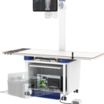 Medical x-ray imaging stand with movable arm and monitoring screen displaying a spine radiograph.