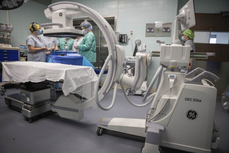 Large medical device over a hospital bed with a group of nurses in the background