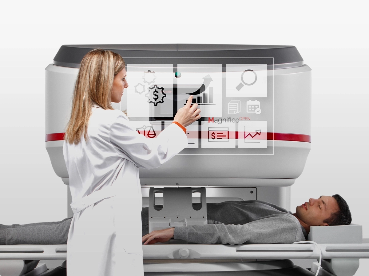 Clinician operates a large medical imaging/treatment machine over a patient lying on a table for radiotherapy or scanning.