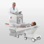 Patient lying on a medical imaging scanner table as a clinician stands beside the machine, preparing for a scan.