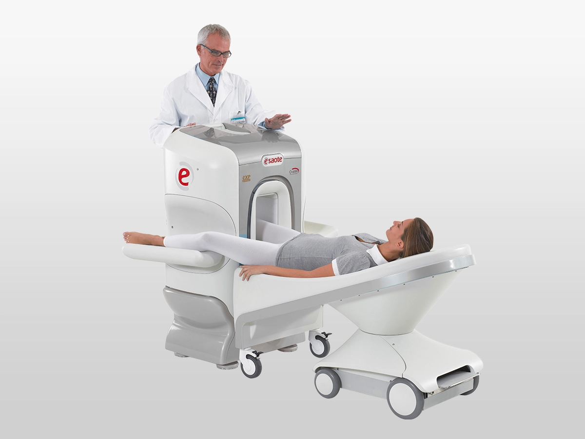Patient lying on a medical imaging scanner table as a clinician stands beside the machine, preparing for a scan.