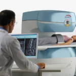 Technician in a white coat operating an mri machine while a patient lies on the scanner table awaiting imaging. A computer monitor shows spinal mri scans nearby.