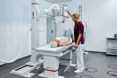 Patient lying on a ct scanner table as a radiologic technologist stands beside, preparing for a scan.